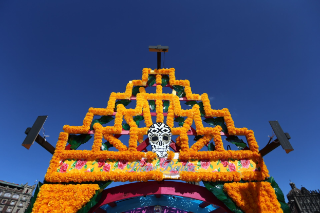 Ein Día de los Muertos-Bogen, geschmückt mit Blumen und einem Schädel, steht in Mexiko-Stadt vor Häusern unter einem klaren blauen Himmel.