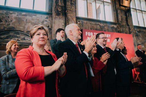 Eine Gruppe von Menschen, die vor einer Menge jubeln, mit einem Banner im Hintergrund, das "Wahlsieg" lautet.
