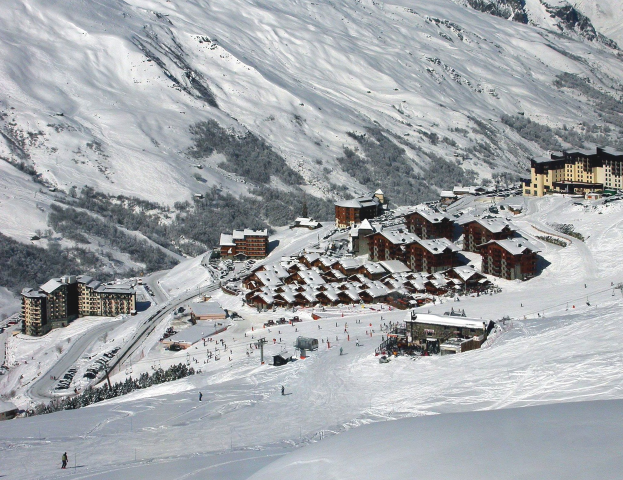 Eine malerische Aussicht auf ein Skigebiet in den französischen Alpen mit schneebedeckten Bergen, Gebäuden, Bäumen und Skifahrern auf den Pisten.