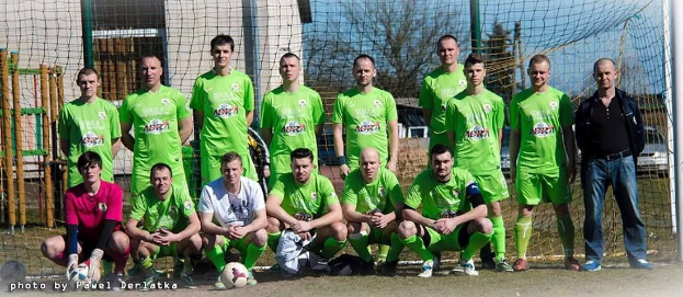 Eine Gruppe von Männern in grünen T-Shirts steht auf einem Fußballfeld mit einem Ball und einem Tor, einige in einer Hockposition.